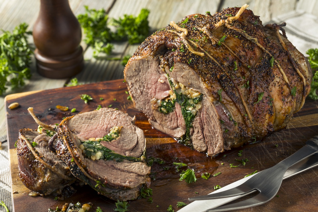 a whole and slices of roasted stuffed lamb leg on a chopping board