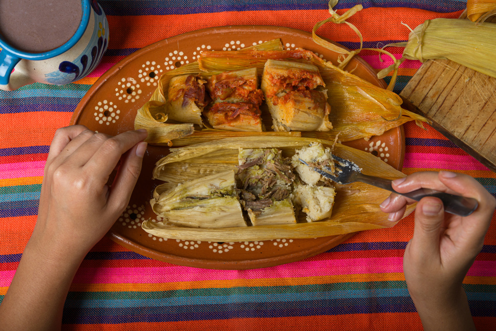 Hands of a person cutting a tamale with a fork