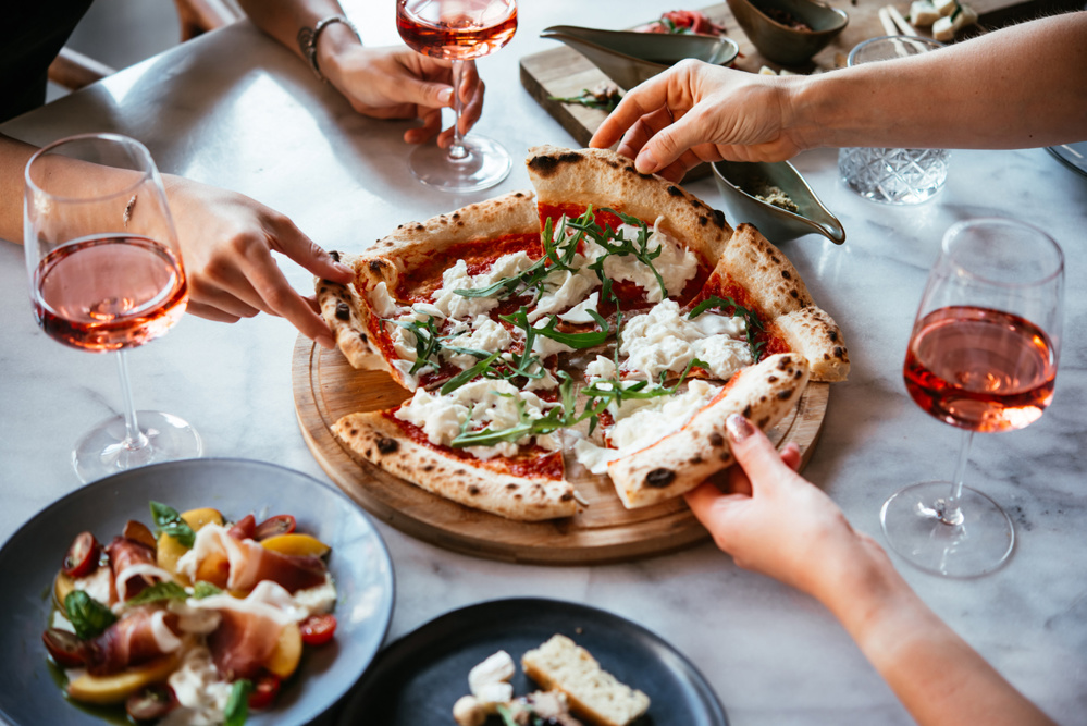 Friends enjoy a dinner party with pizza and rose wine in a bar or a restaurant