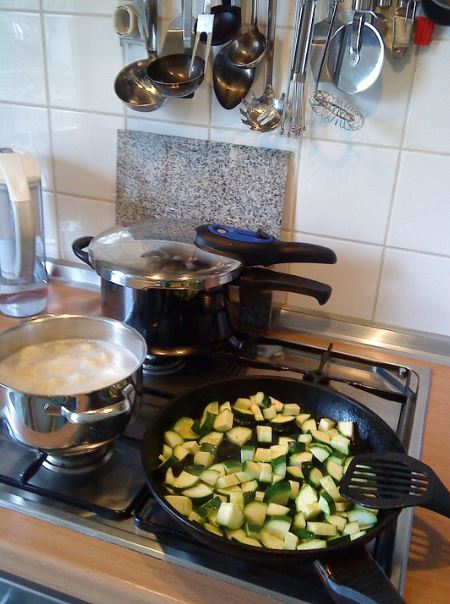 a stove with a pressure cooker, pot with boiling water, pan with vegetables